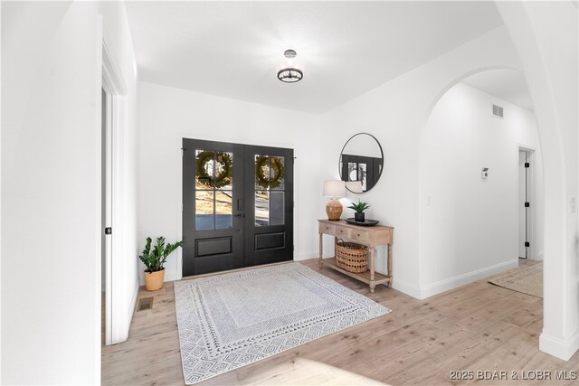 entryway with arched walkways, wood finished floors, baseboards, and french doors