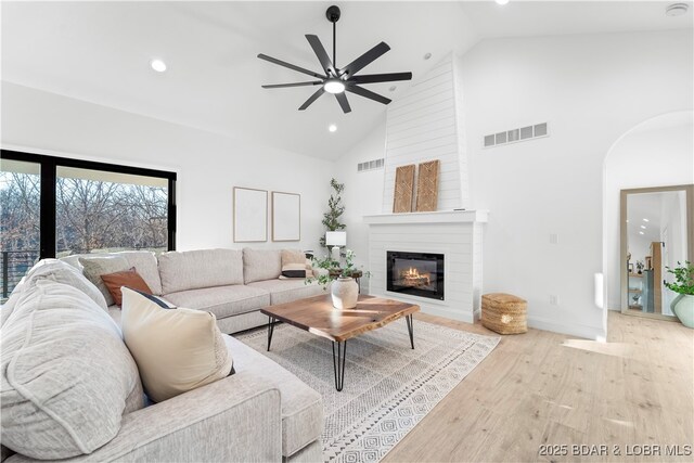 living room with a ceiling fan, high vaulted ceiling, a large fireplace, wood finished floors, and arched walkways