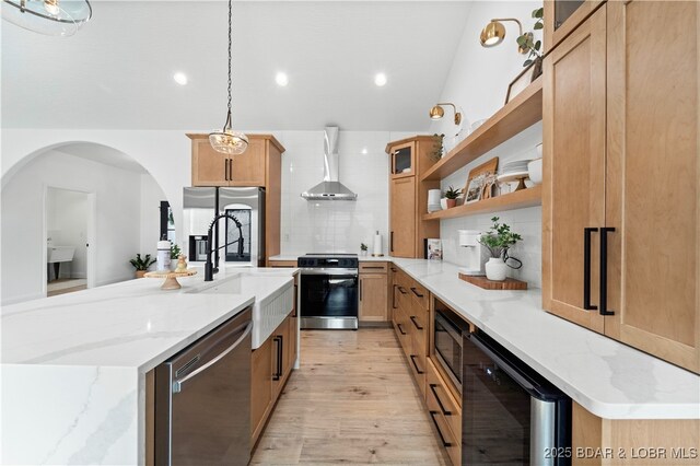 kitchen with stainless steel appliances, wall chimney exhaust hood, open shelves, light wood-type flooring, and decorative backsplash