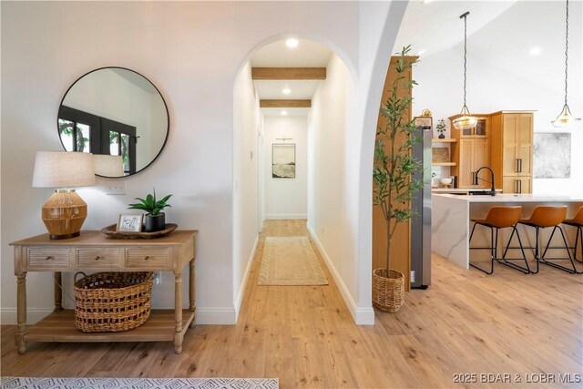 hall with arched walkways, light wood-style floors, a sink, baseboards, and recessed lighting