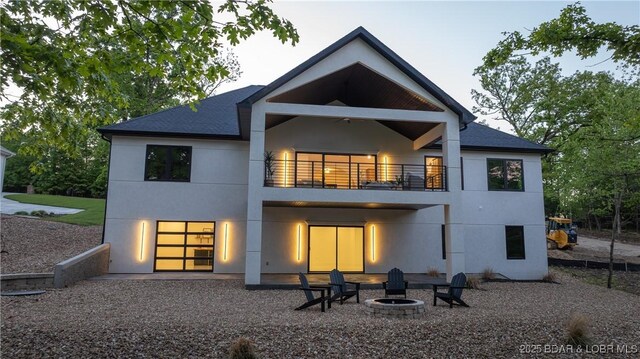 rear view of property featuring a balcony, stucco siding, a fire pit, and a shingled roof