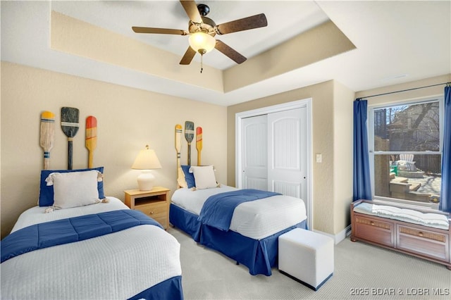 bedroom with light colored carpet, a tray ceiling, a closet, and a ceiling fan