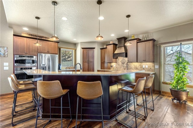 kitchen featuring custom exhaust hood, stainless steel appliances, a textured ceiling, tasteful backsplash, and a spacious island