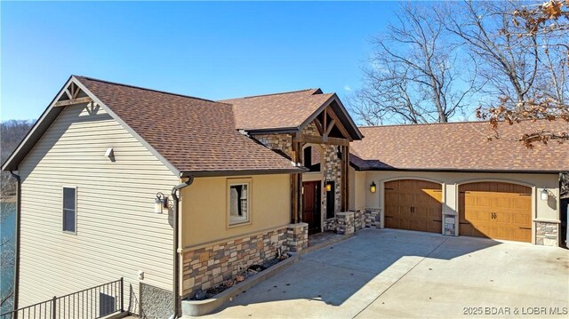 view of front of property featuring stone siding, concrete driveway, an attached garage, and roof with shingles