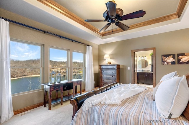 carpeted bedroom with a tray ceiling, baseboards, connected bathroom, and a water view