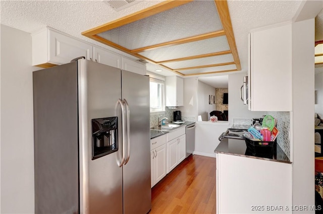 kitchen featuring dark countertops, a sink, light wood-style flooring, stainless steel appliances, and white cabinetry