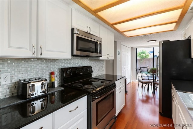 kitchen with dark wood-style flooring, appliances with stainless steel finishes, white cabinetry, and tasteful backsplash