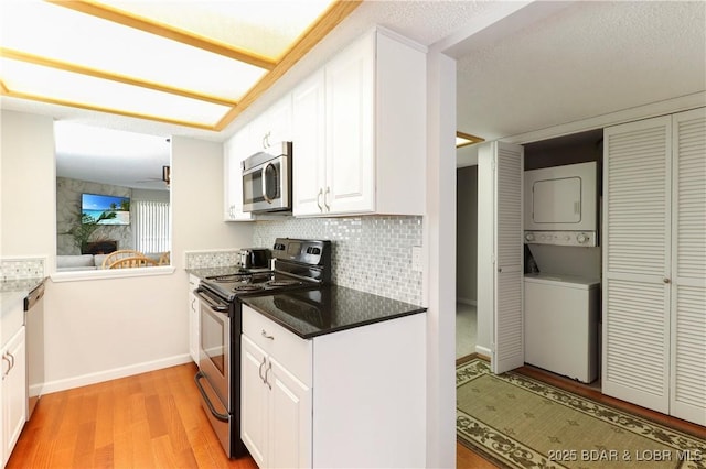 kitchen with backsplash, light wood-style floors, white cabinetry, appliances with stainless steel finishes, and stacked washer / drying machine