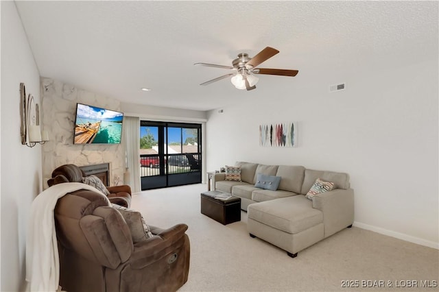 living area featuring carpet floors, ceiling fan, a stone fireplace, and visible vents