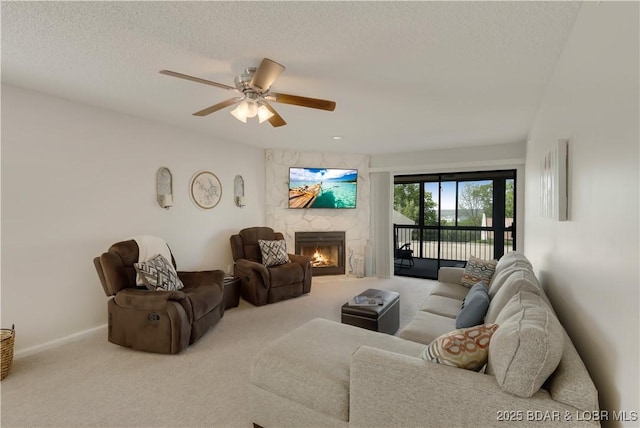 living area with a ceiling fan, a textured ceiling, a large fireplace, carpet floors, and baseboards