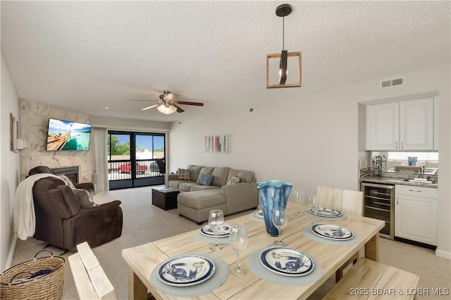 dining room featuring visible vents, light carpet, beverage cooler, ceiling fan, and a textured ceiling