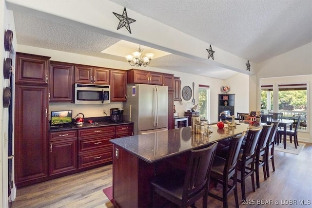 kitchen with light wood finished floors, lofted ceiling, an inviting chandelier, stainless steel appliances, and reddish brown cabinets