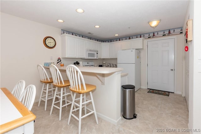 686 Clearwater Dr Unit 1E, Camdenton, MO 65020 - kitchen with white appliances, a peninsula, a kitchen bar, recessed lighting, and white cabinets