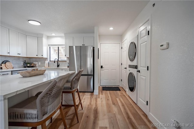 611 Lazy Days Rd Unit F5, Osage Beach, MO 65065 - kitchen featuring white cabinets, freestanding refrigerator, stacked washing maching and dryer, light wood-style flooring, and tasteful backsplash
