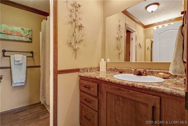 bathroom with vanity, a textured ceiling, wood finished floors, visible vents, and ornamental molding