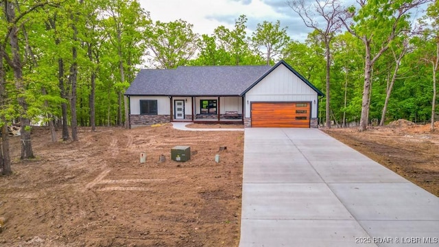 view of front of property featuring stone siding, covered porch, concrete driveway, and an attached garage