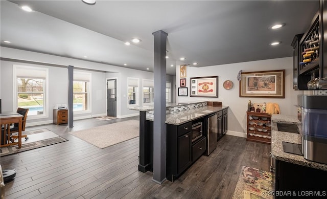 kitchen featuring light stone countertops, dark cabinetry, dark wood-type flooring, open floor plan, and recessed lighting