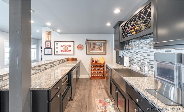 kitchen featuring light stone countertops, stainless steel dishwasher, a sink, light wood-type flooring, and backsplash