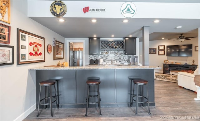 kitchen with decorative backsplash, a breakfast bar, dark wood finished floors, light stone counters, and freestanding refrigerator