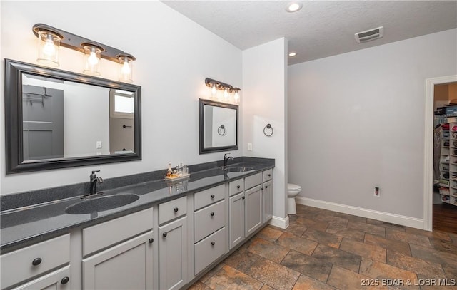 bathroom with baseboards, visible vents, double vanity, and a sink