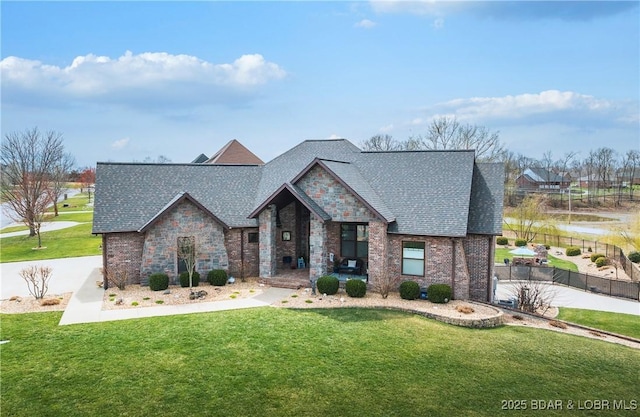 view of front of home with roof with shingles, brick siding, a front yard, and fence