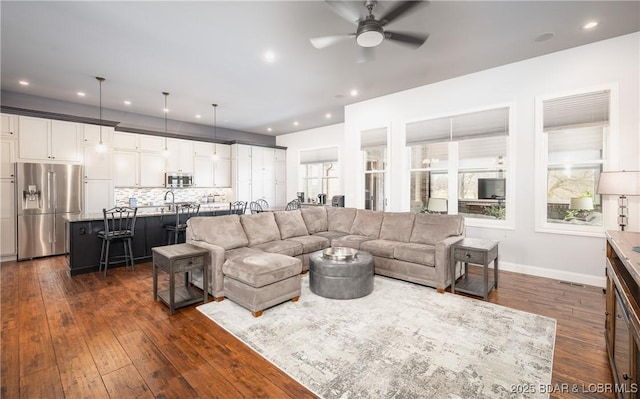 living area featuring baseboards, dark wood-style flooring, ceiling fan, and a wealth of natural light