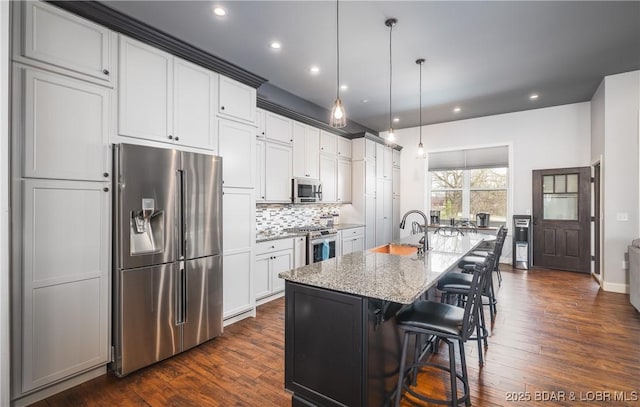 kitchen featuring backsplash, a center island with sink, a sink, light stone counters, and appliances with stainless steel finishes