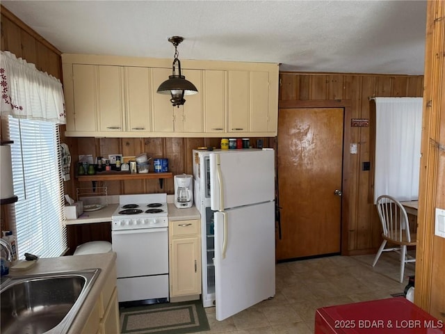 kitchen featuring white appliances, wooden walls, light countertops, and a sink