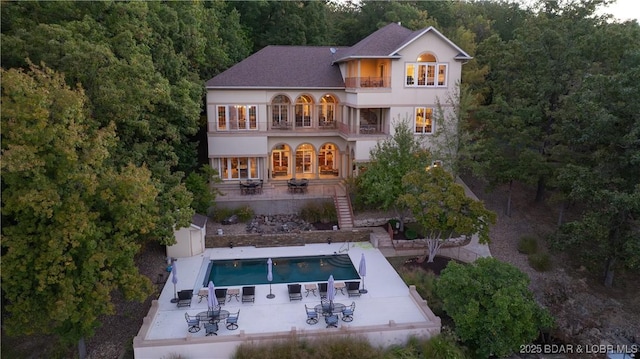 rear view of property featuring an outdoor pool, stucco siding, stairway, a balcony, and a patio area
