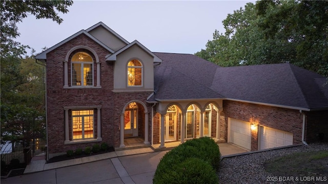 traditional-style home featuring driveway, brick siding, a garage, and roof with shingles