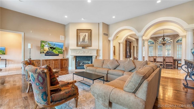 living area featuring decorative columns, a glass covered fireplace, light wood-style floors, and visible vents