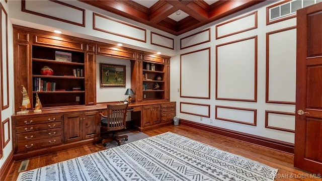 unfurnished office featuring coffered ceiling, built in shelves, dark wood-style floors, beamed ceiling, and built in desk