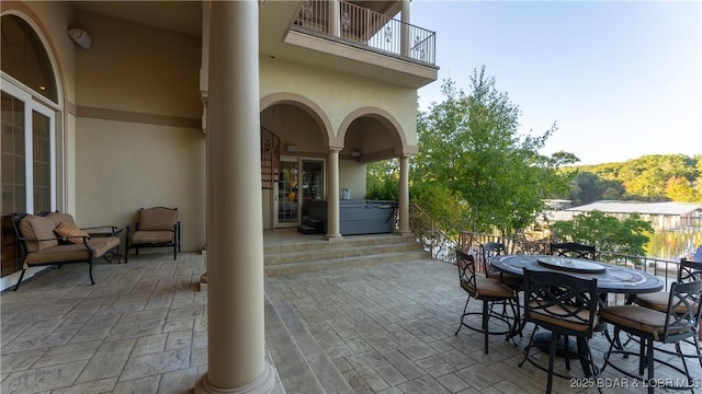 view of patio with a hot tub, outdoor dining space, and a balcony