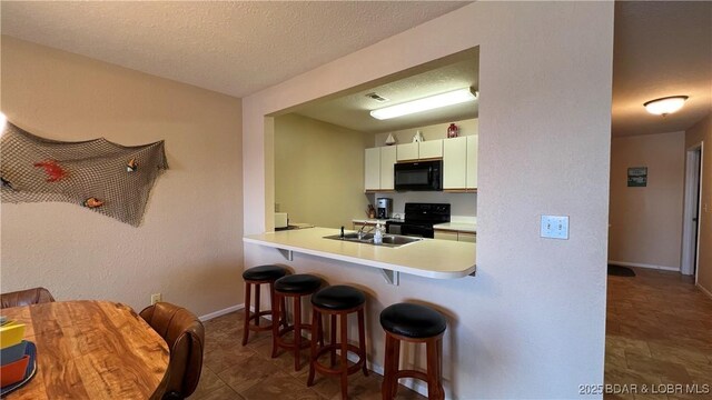 31347 Northshore Dr Unit 101A, Rocky Mount, MO 65072 - kitchen with a textured ceiling, white cabinets, light countertops, a kitchen bar, and black appliances