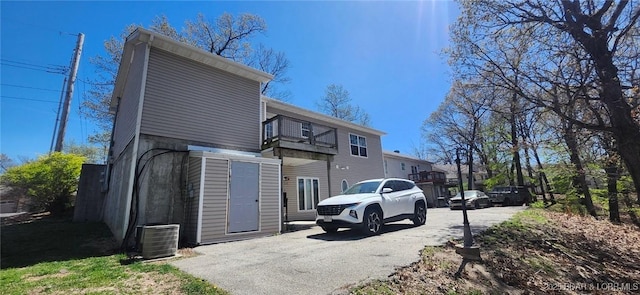 back of house with aphalt driveway, central AC unit, and a balcony