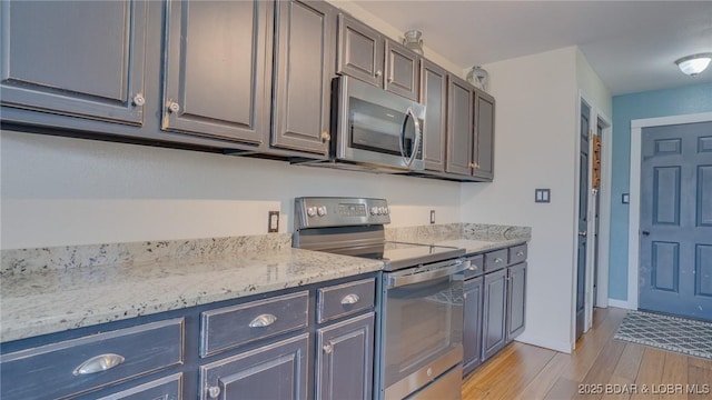 kitchen featuring light stone counters, stainless steel appliances, light wood finished floors, and baseboards