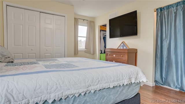 bedroom featuring baseboards, visible vents, wood finished floors, and a closet