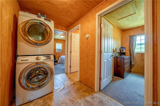 laundry area featuring carpet floors, wood walls, stacked washing maching and dryer, and laundry area