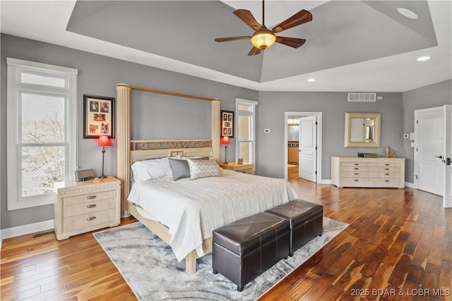 bedroom with a raised ceiling, baseboards, hardwood / wood-style flooring, recessed lighting, and multiple windows