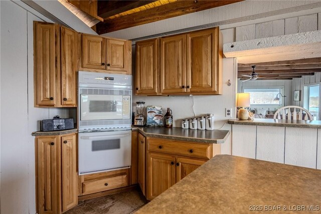 33271 Elaine Rd, Sunrise Beach, MO 65079 - kitchen with white double oven, beam ceiling, brown cabinets, a ceiling fan, and dark countertops