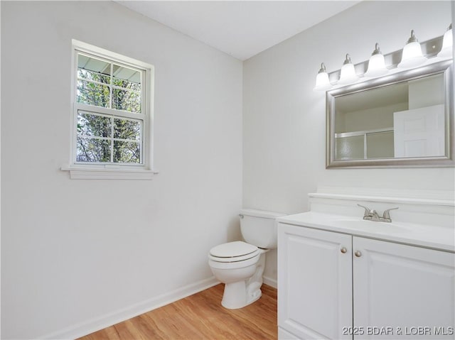 bathroom with an enclosed shower, wood finished floors, baseboards, vanity, and toilet