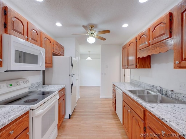 kitchen with a sink, light countertops, light wood-type flooring, and white appliances