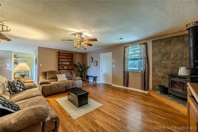 living area with baseboards, a textured ceiling, a wood stove, ceiling fan, and wood-type flooring