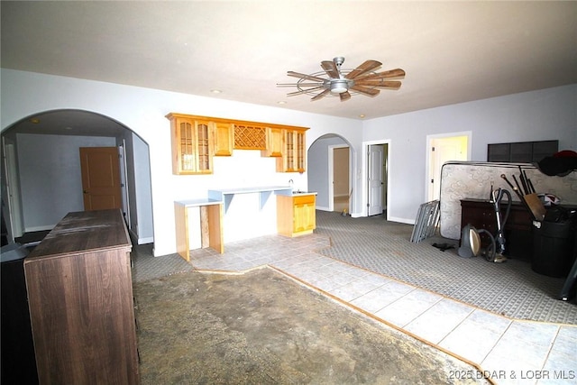 kitchen featuring ceiling fan, glass insert cabinets, carpet, arched walkways, and open floor plan