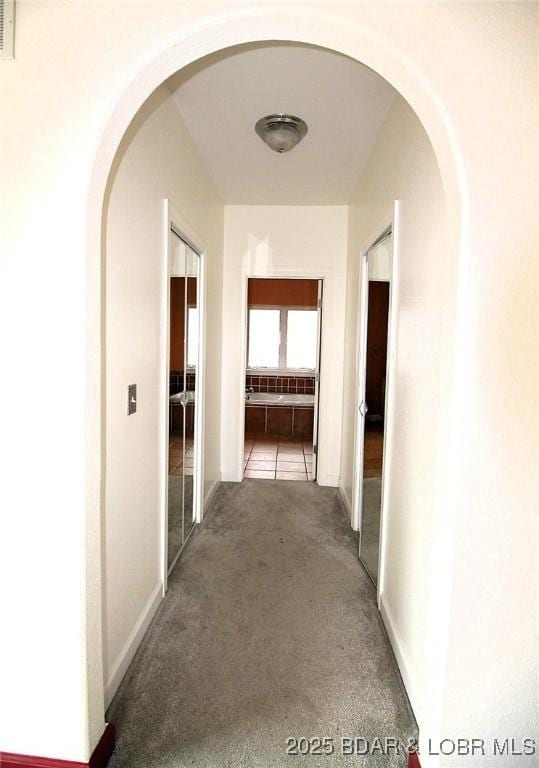 hallway featuring arched walkways, carpet flooring, visible vents, and baseboards