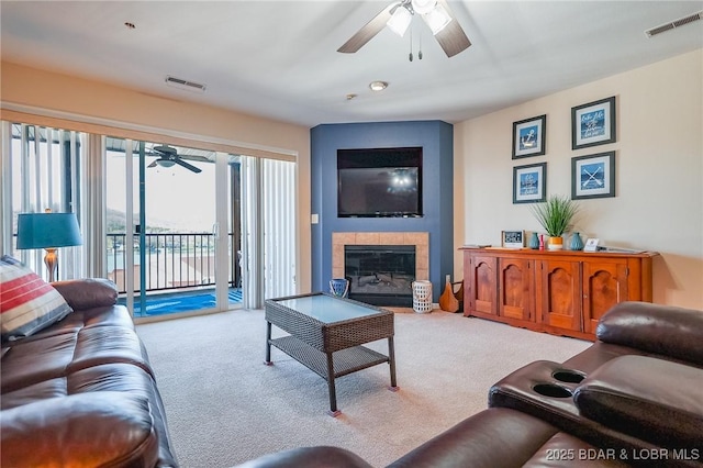 carpeted living room featuring a large fireplace, visible vents, and ceiling fan