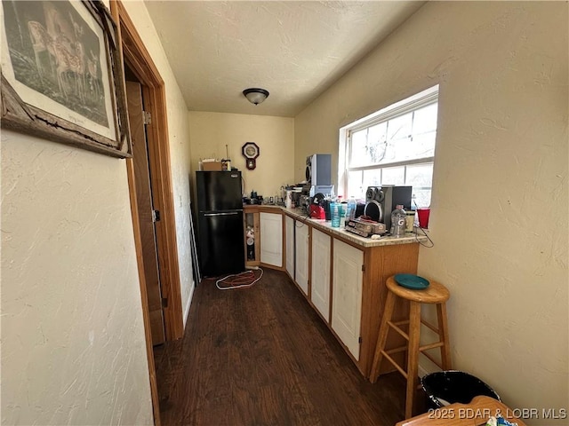 kitchen featuring a textured wall, dark wood-style floors, and freestanding refrigerator
