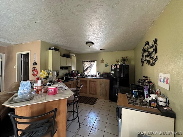 kitchen with a kitchen breakfast bar, a peninsula, a textured ceiling, freestanding refrigerator, and light tile patterned flooring