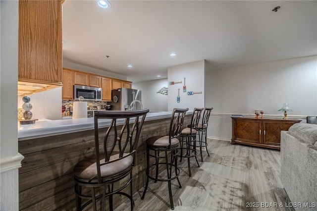 251 Vision Dr Unit 1D, Camdenton, MO 65020 - kitchen with light wood-type flooring, recessed lighting, a breakfast bar area, decorative backsplash, and appliances with stainless steel finishes
