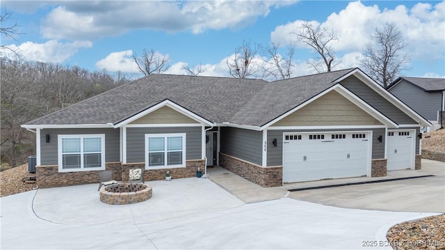 craftsman-style house with an attached garage, concrete driveway, stone siding, and a fire pit